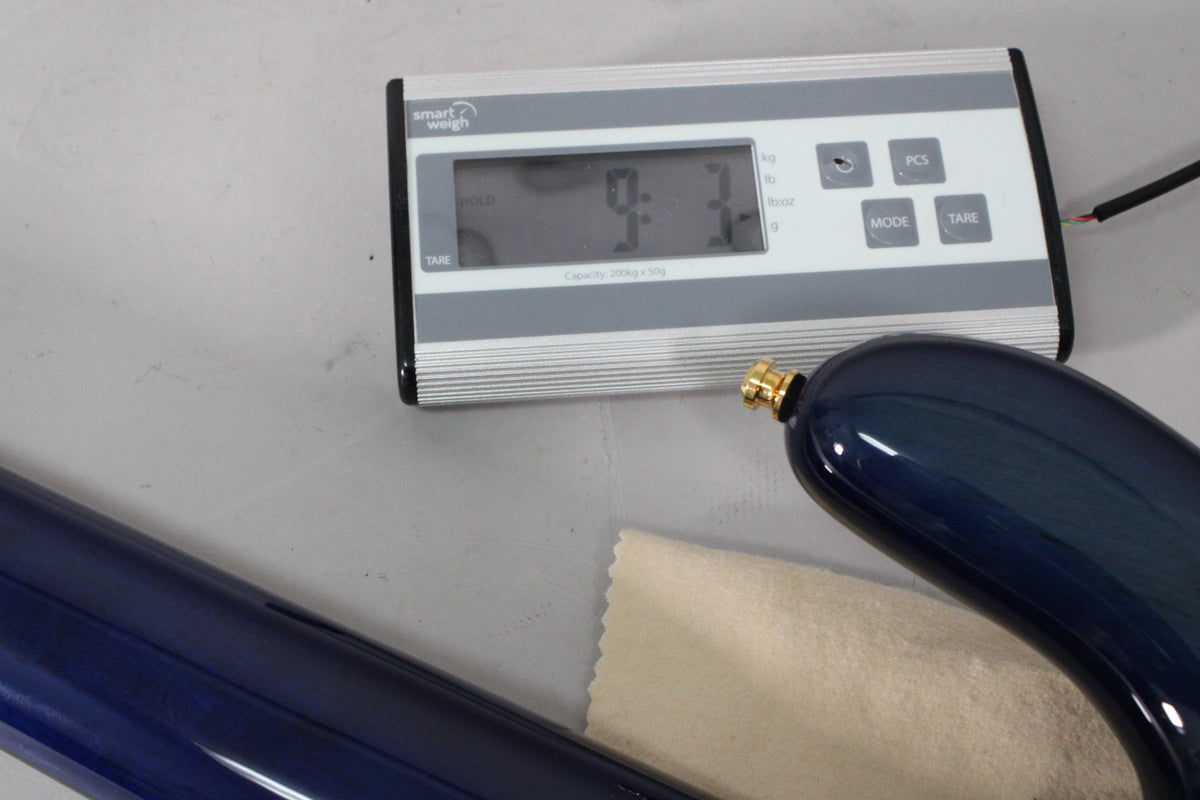 The bass guitar's dark blue gloss body with a gold strap button is visible next to a digital scale displaying "9.3" lbs.