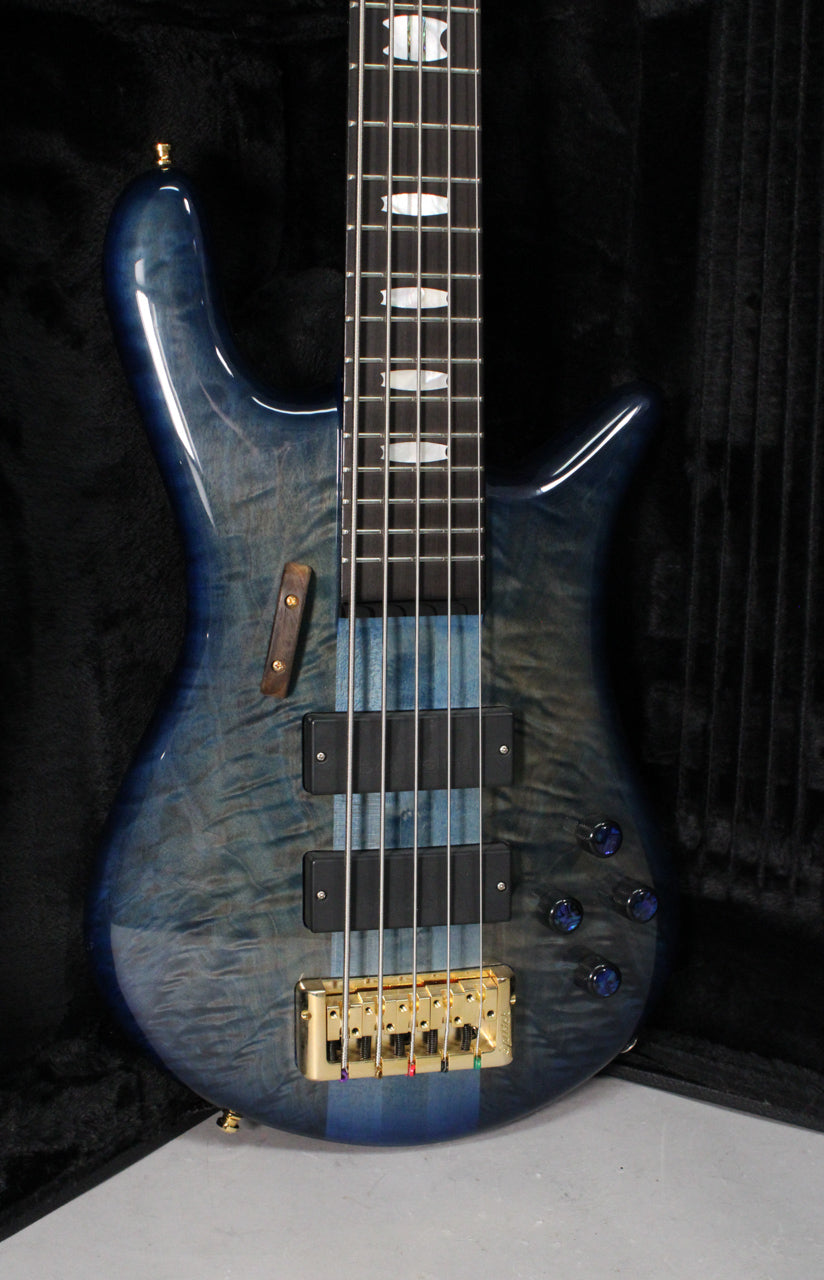 The blue fade gloss bass guitar is angled, showing its body, gold bridge, two black pickups, and part of the fretboard.