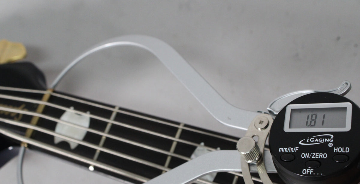 Close-up of the bass fretboard with pearloid inlays, showing a digital caliper measuring the string height at 1.81mm.