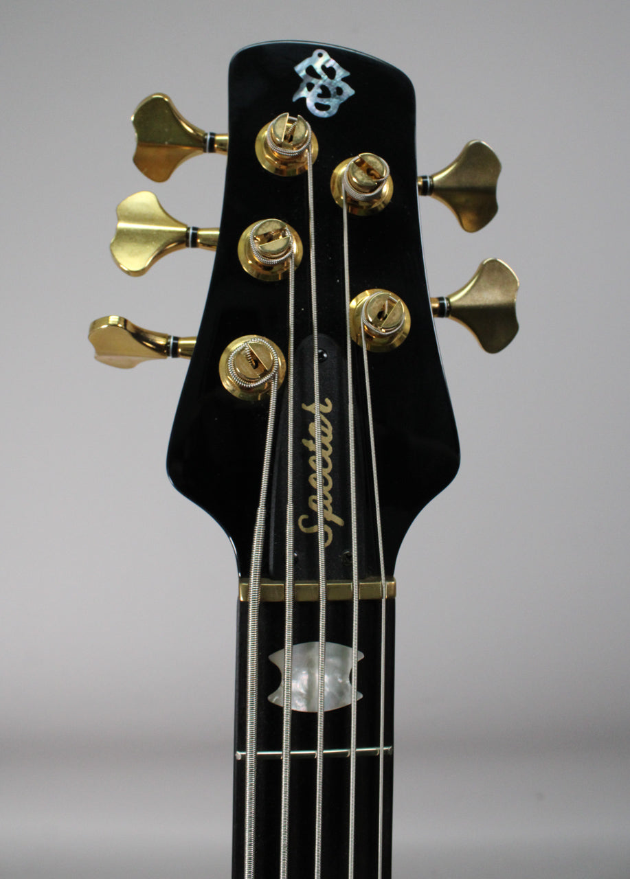 The black gloss headstock with gold tuners and a mother-of-pearl inlay is viewed from the front, showing the top of the fretboard.