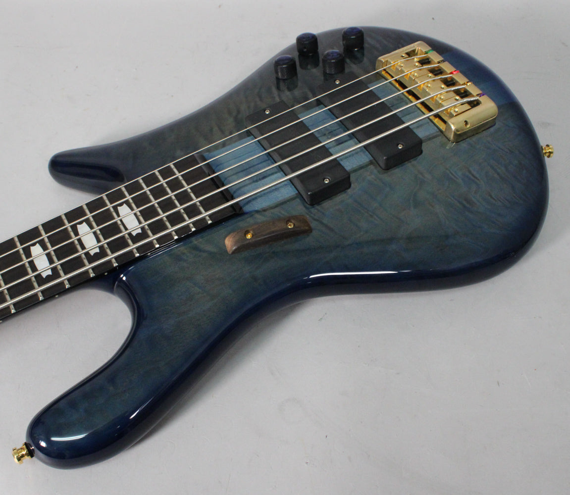 Close-up of a blue fade gloss bass guitar, showing the upper body, gold bridge, black pickups, and part of the fretboard with block inlays.