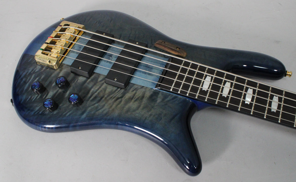 The bass guitar's upper body, with a blue fade gloss finish, gold bridge, four blue-swirl control knobs, and mother-of-pearl fret inlays.