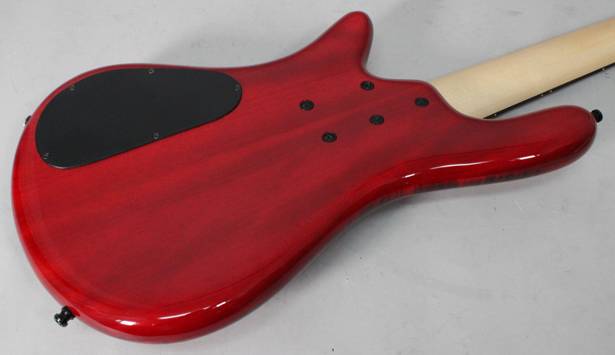 The back of a cherry red bass guitar with a black control plate, four black neck bolts, and a light wood neck.