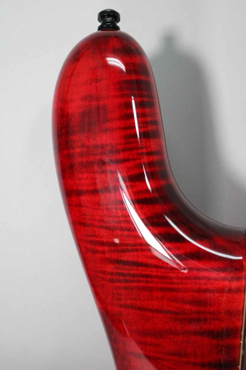 Close-up of the bass's upper horn, showing the glossy black cherry flame finish with subtle surface scratches and a black strap button.