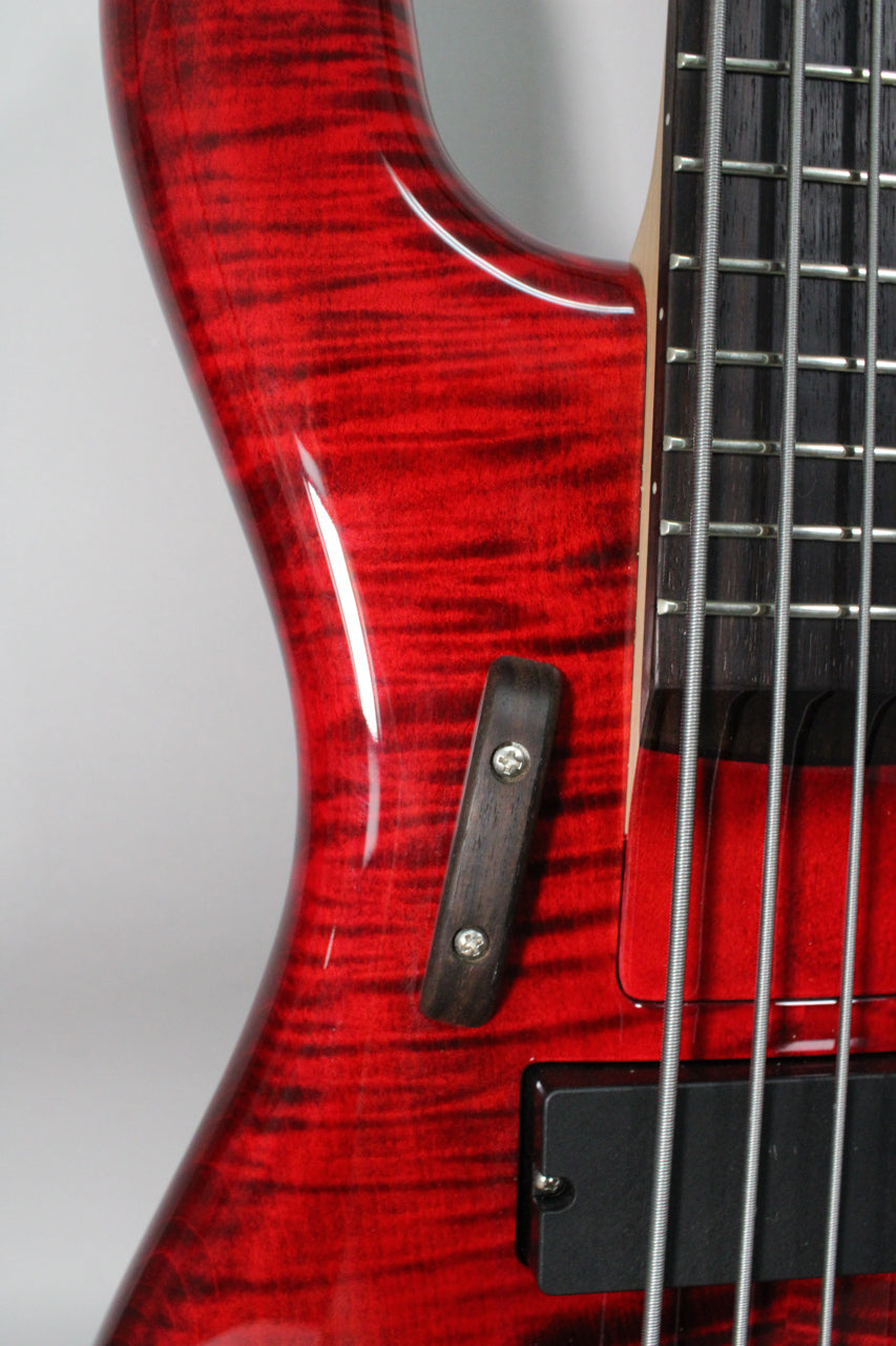 Close-up of the bass body's upper bout in glossy black cherry flame, showing a dark wood ramp between the neck and a black pickup.