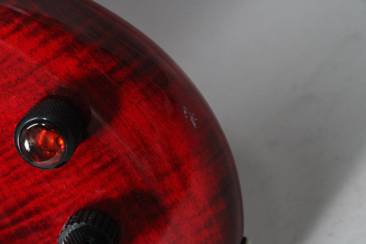 Close-up of the bass's upper body, showing the black cherry flame finish, two black knurled knobs, and a small ding.