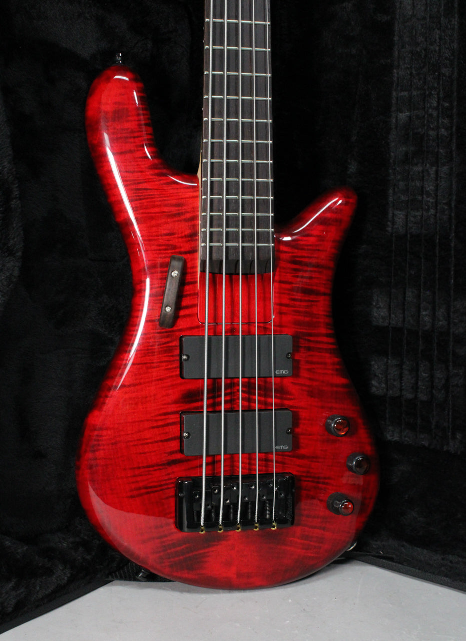 The bass guitar's upper body and neck are angled, showing the glossy black cherry flame finish, two black EMG pickups, and black hardware.