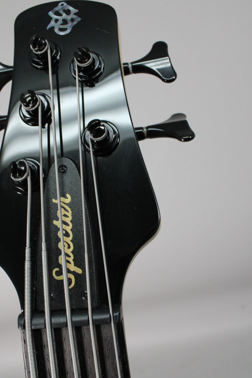 Close-up of the glossy black headstock with five black tuners, a pearloid inlay, and gold lettering on the truss rod cover.