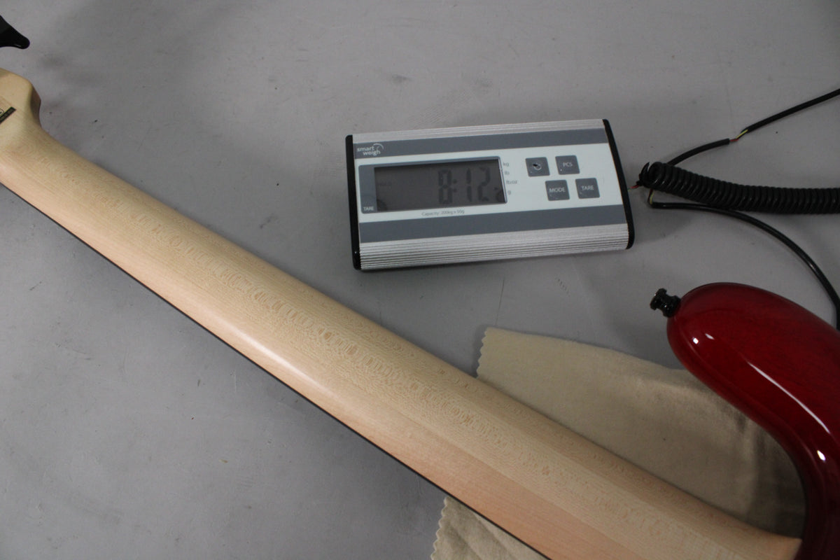 The bass neck, light wood with a dark stripe, extends from a cherry flame body, with a digital scale showing "8.12" in the background.