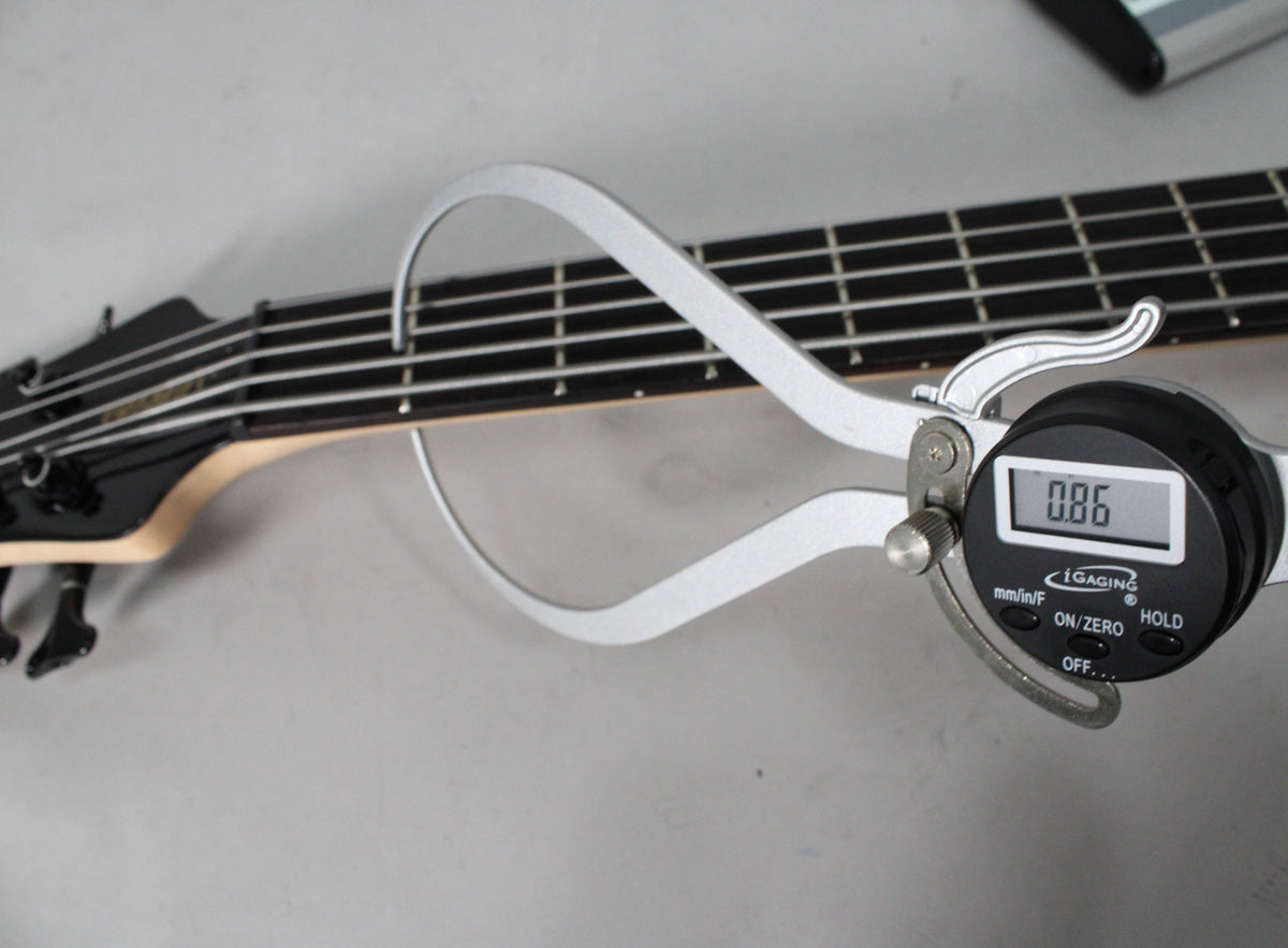 A digital caliper measures the bass's black fretboard and five strings, displaying "0.86" on its screen.