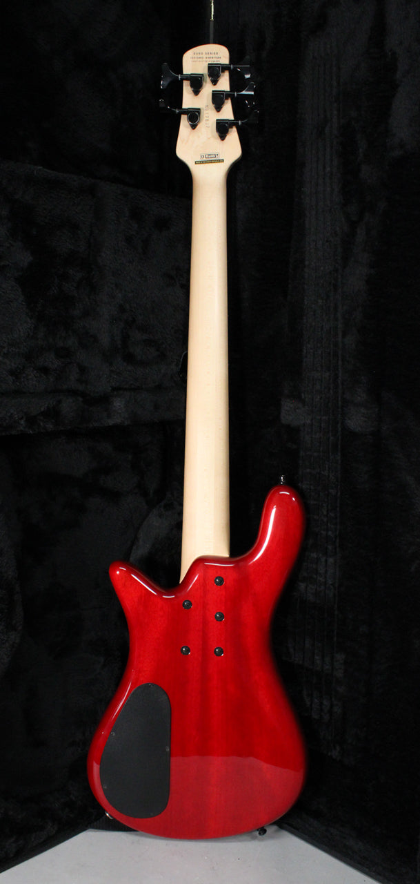 The back of a cherry flame bass, showing the light wood neck, black tuners, and a black control cavity cover.