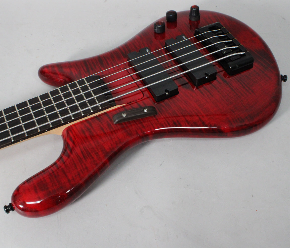 The upper half of a glossy red flame maple bass, angled left, showing black pickups, bridge, and control knobs.