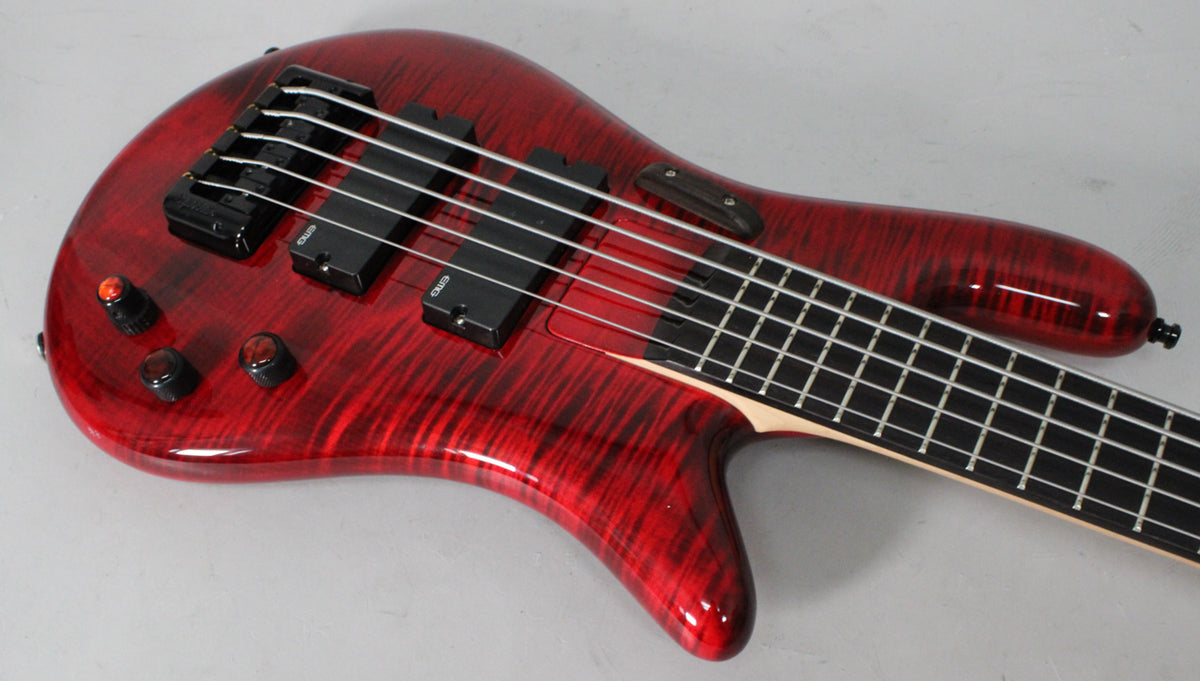 The bass guitar's upper body and neck are angled right, showing its glossy cherry flame finish, black hardware, and four control knobs.