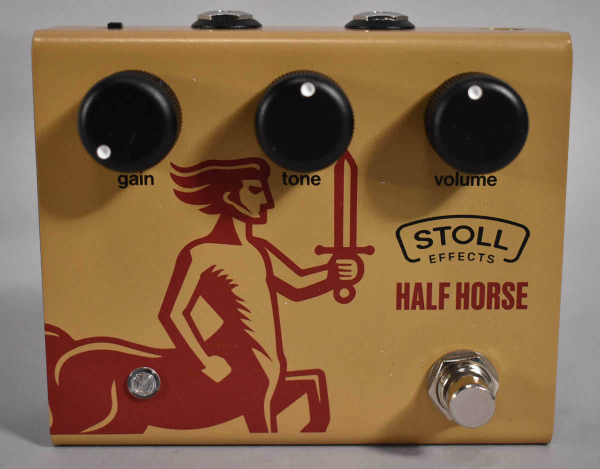 The gold pedal has three black control knobs labeled "gain," "tone," and "volume," a red centaur graphic, and a chrome footswitch.