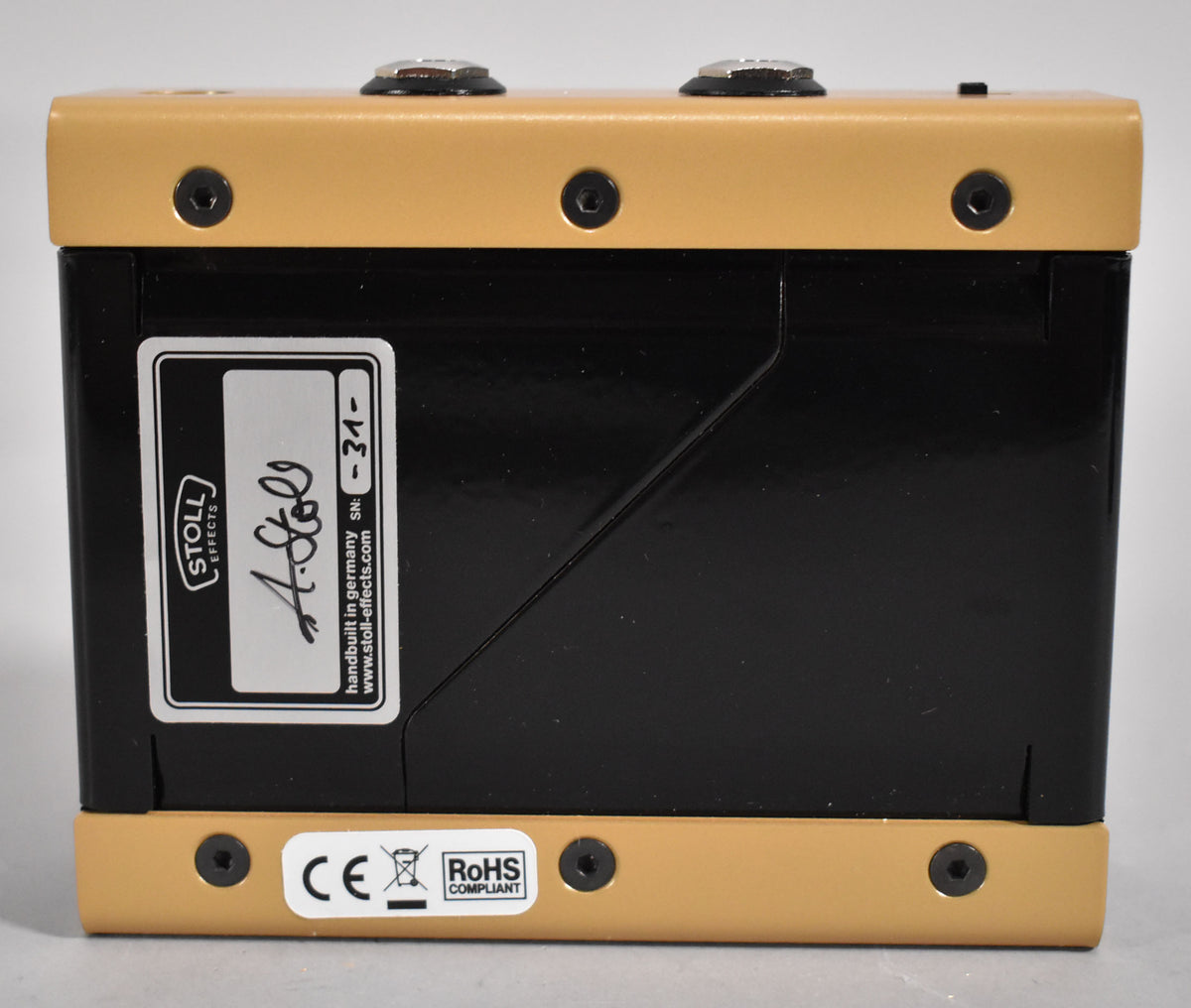 The Stoll Effects Half Horse Overdrive Pedal, viewed from the rear, features a black body with gold top and bottom plates, secured by black hex screws.