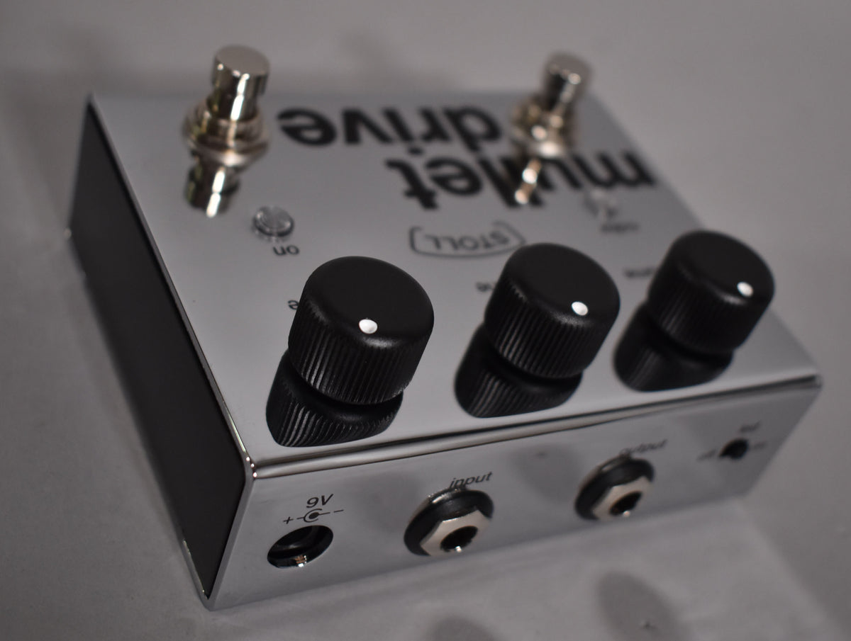Chrome pedal, angled from the front-right, showing three black knobs, two footswitches, and input/output jacks.