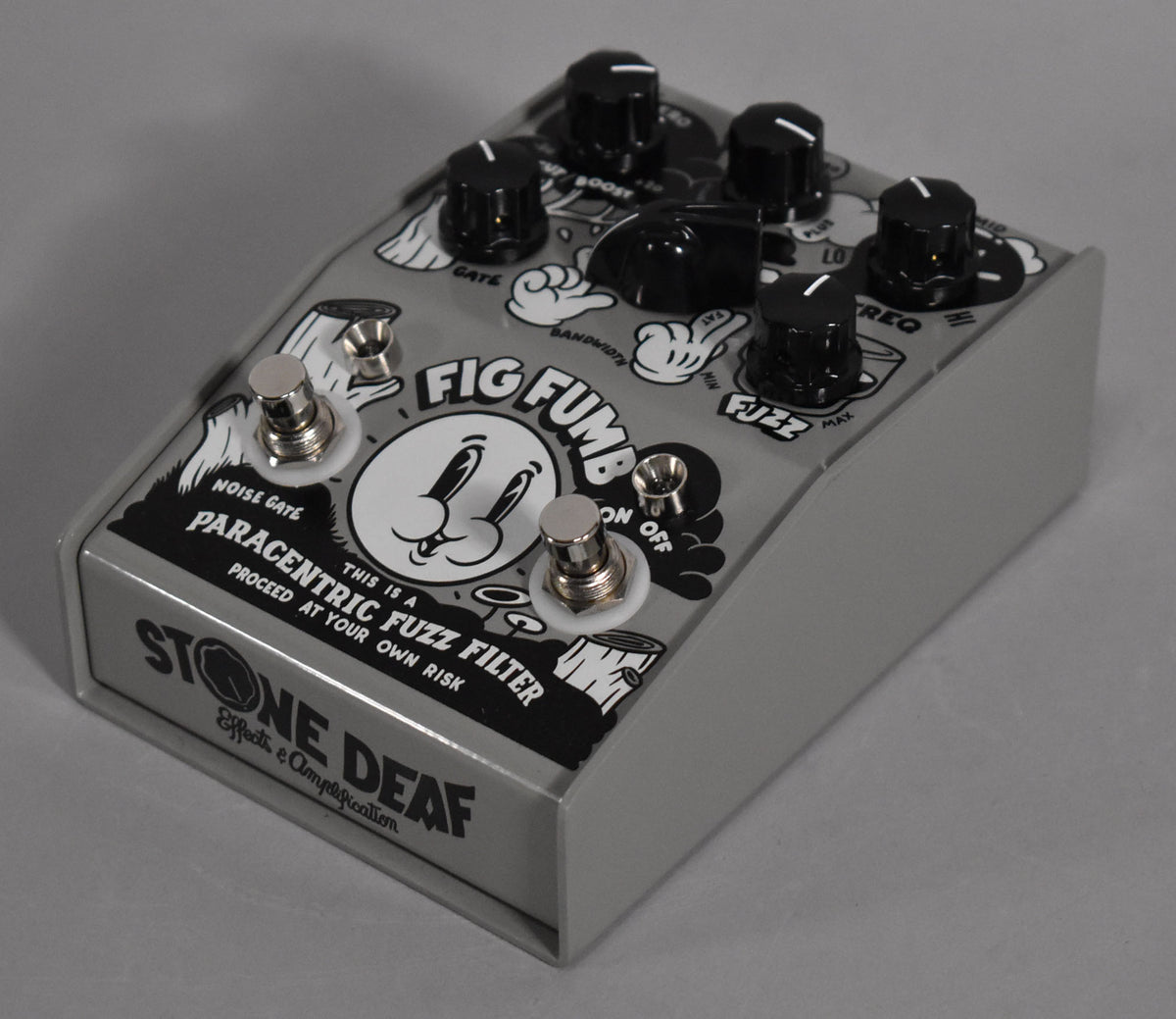 A light gray guitar pedal with black knobs and footswitches, featuring a cartoon face and hands graphic.