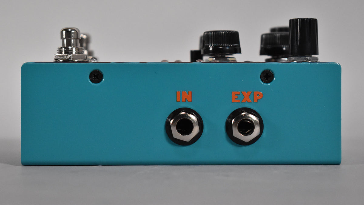 The teal pedal's right side shows two input jacks labeled "IN" and "EXP" in orange, with black control knobs visible on top.