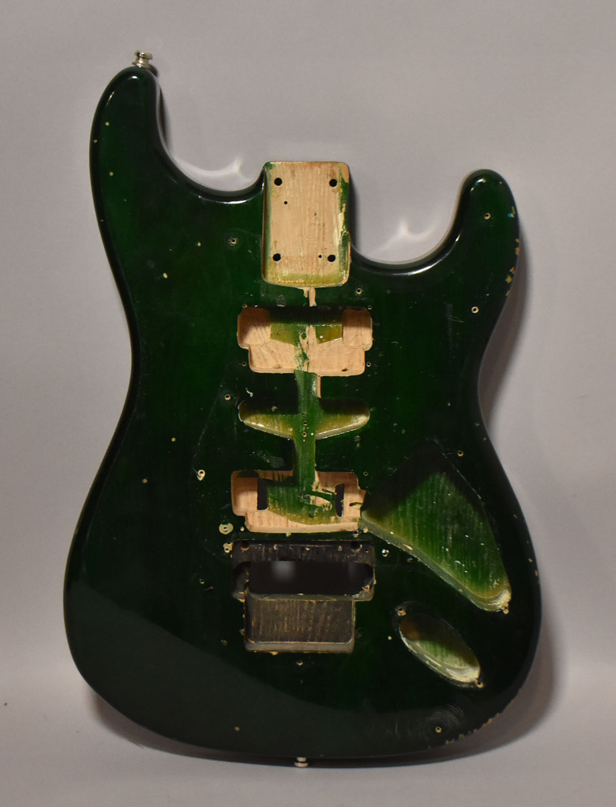 Full-front view of a dark green S-style guitar body with HSH routing, a Floyd Rose tremolo cavity, and visible finish wear.