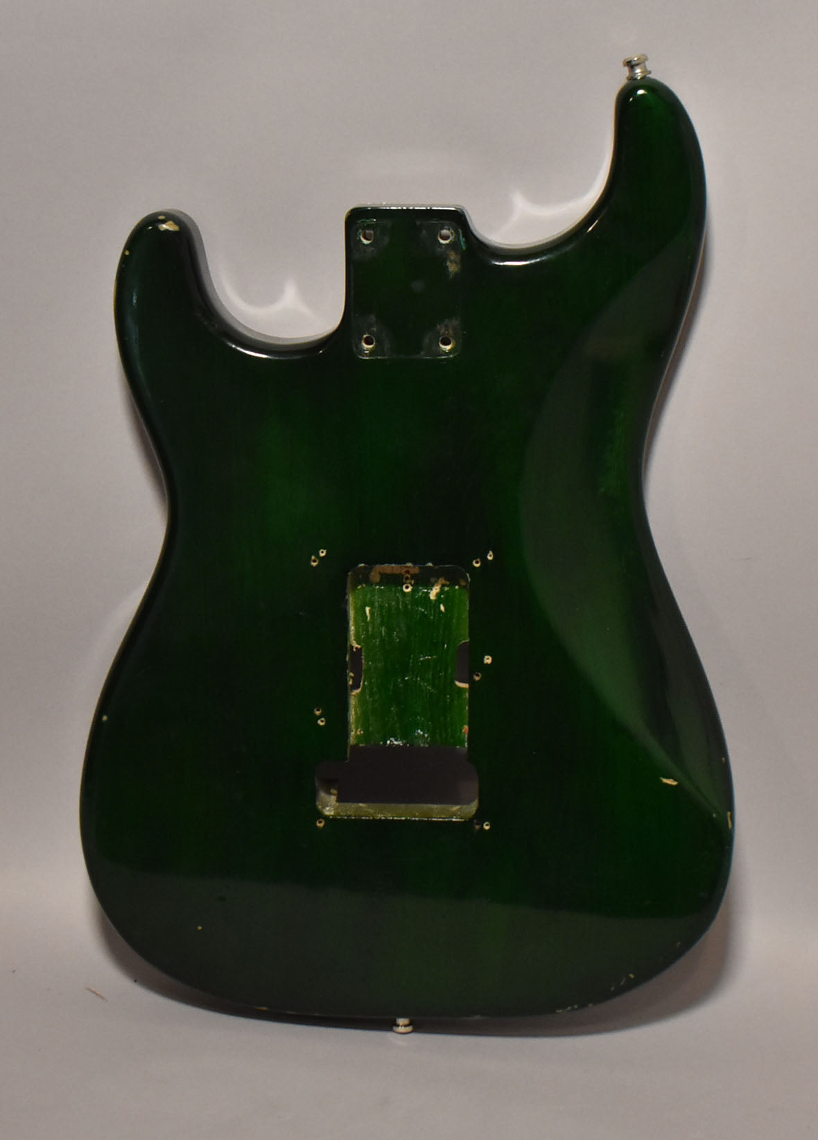 The back of a translucent green S-style guitar body, showing the neck pocket, tremolo cavity, and strap buttons.