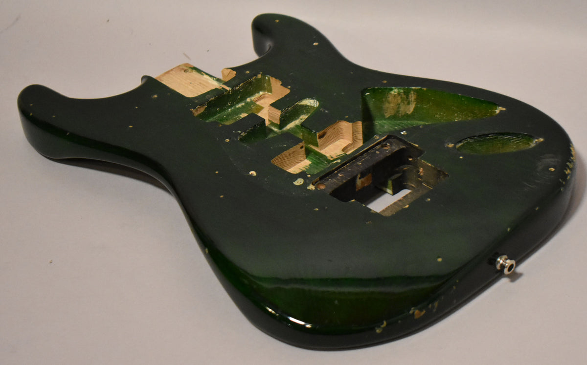 The translucent green S-style guitar body is angled, showing the HSH routing, Floyd Rose cavity, and output jack, with visible finish wear.