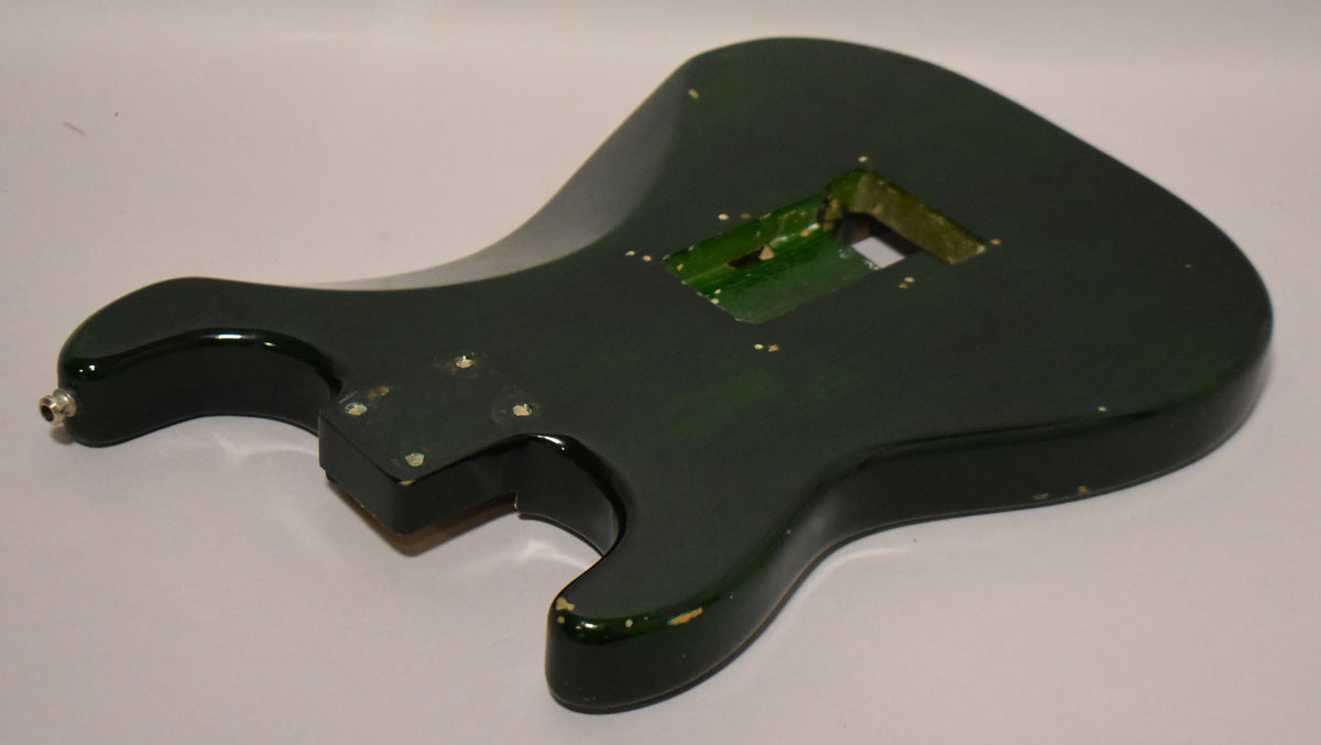 The back of a dark green S-style guitar body, showing a large tremolo cavity and significant paint chipping along the edges.