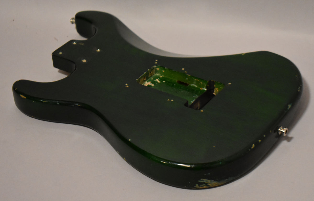 The translucent green S-style guitar body is shown from the back, revealing the tremolo cavity and significant paint chipping.