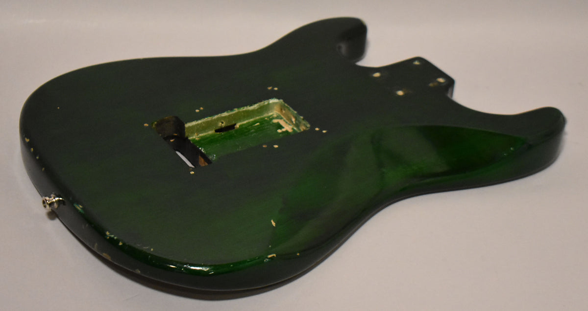 Dark green S-style guitar body, angled from above, showing the back with a Floyd Rose tremolo route and visible wear.