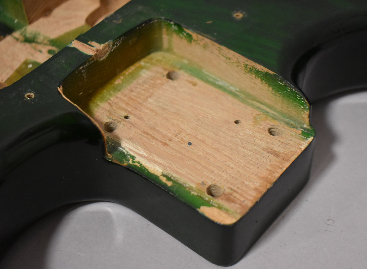 Close-up of the translucent green guitar body's neck pocket, showing exposed wood, screw holes, and paint chipping along the edges.