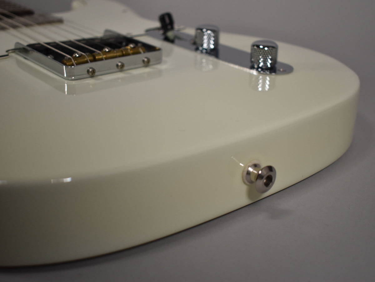 Close-up of the guitar's lower body, showing the Olympic White finish, chrome bridge, control knobs, and output jack.
