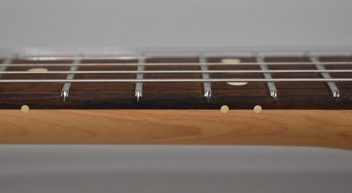Close-up of the guitar's dark rosewood fretboard with light fret markers and side dots, showing the frets and strings.