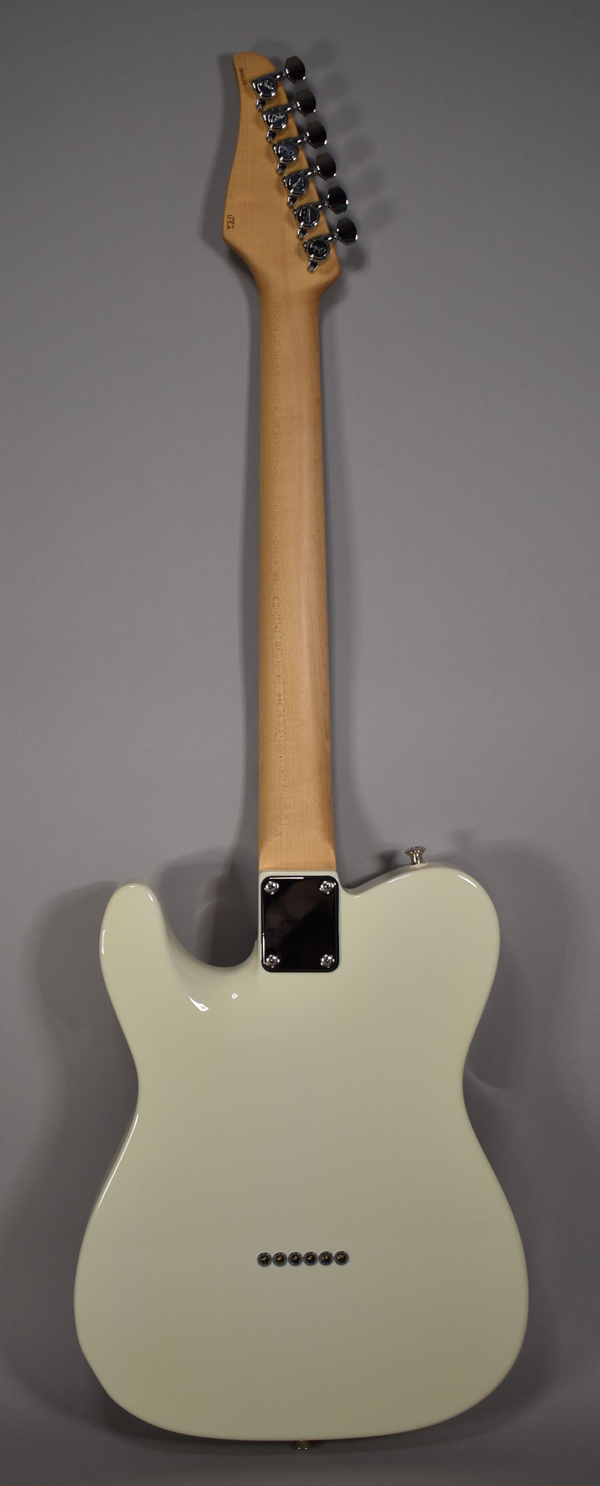 The back of an Olympic White solidbody electric guitar with a maple neck, chrome tuners, and string-through-body ferrules.
