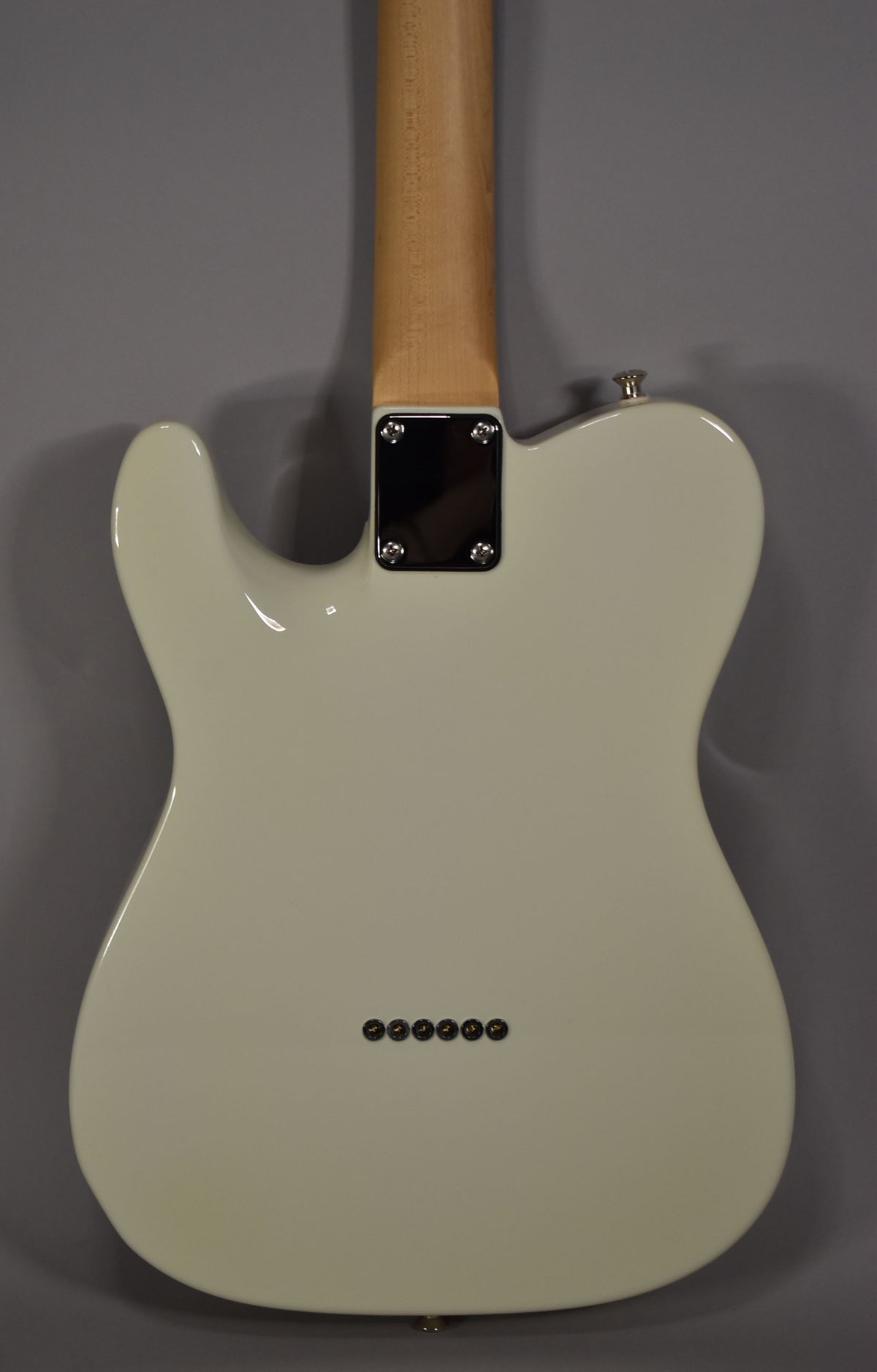 Rear view of an Olympic White solidbody electric guitar with a maple neck, chrome neck plate, and six string-through-body ferrules.