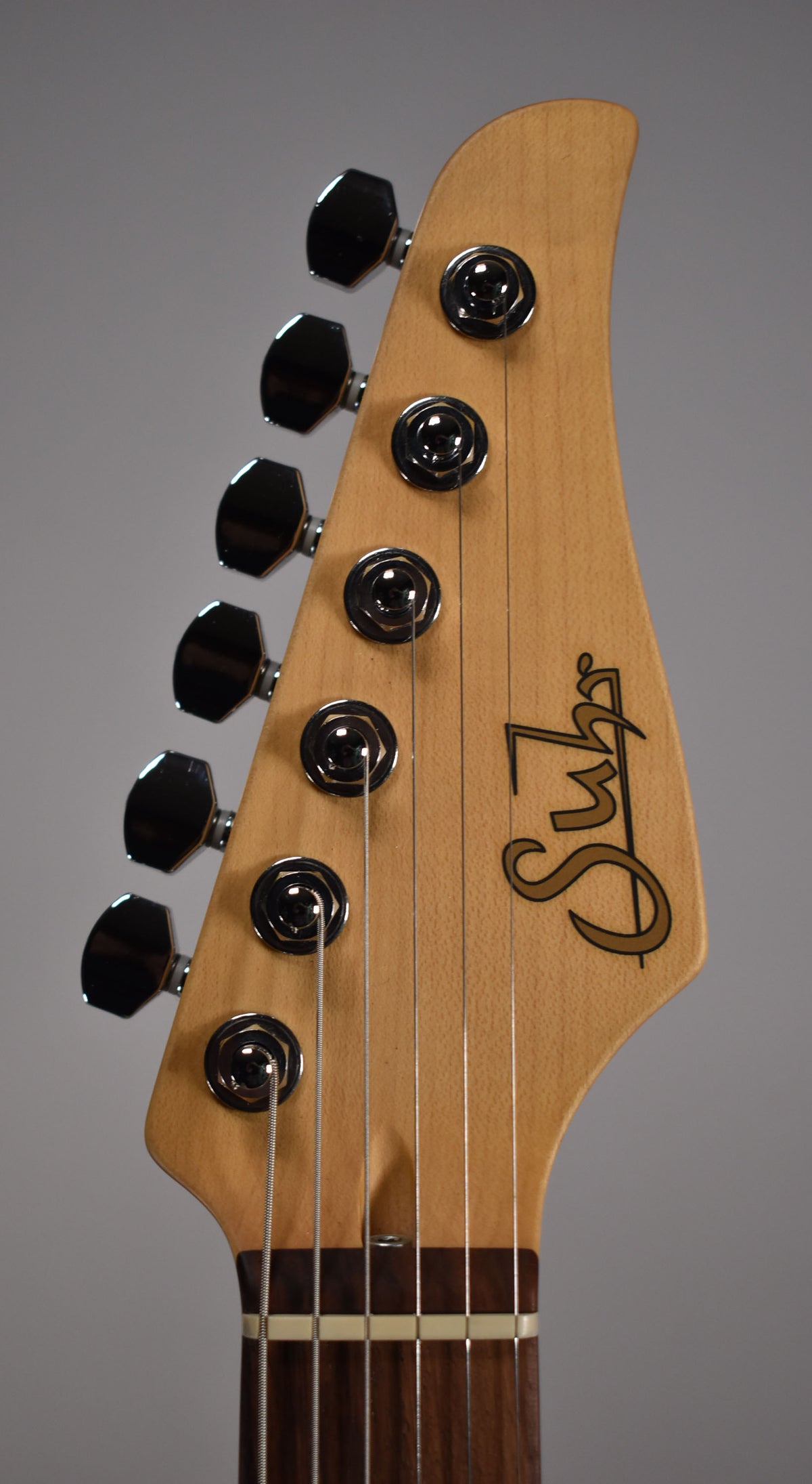 Close-up of the guitar's light wood headstock, angled left, showing six chrome tuners and a dark brown fretboard with a white nut.