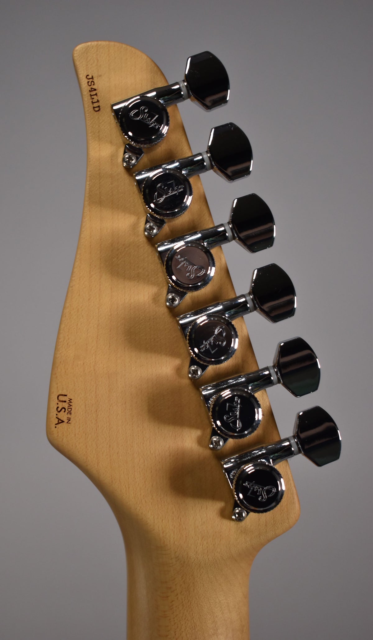 The back of the guitar's headstock, angled slightly from the left, shows six chrome tuners on a light wood finish.