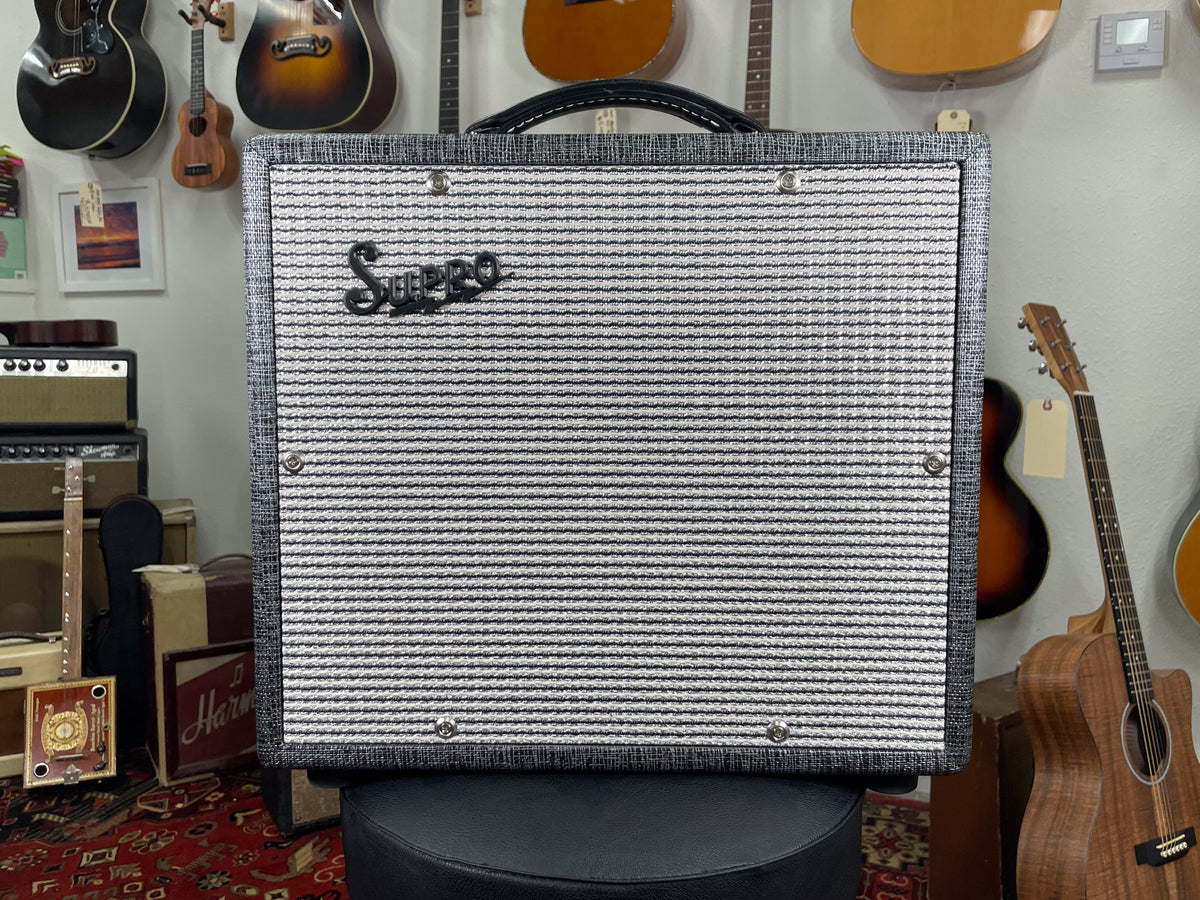 Front view of a gray tweed combo amp with a black and white striped grille cloth and a black top handle.