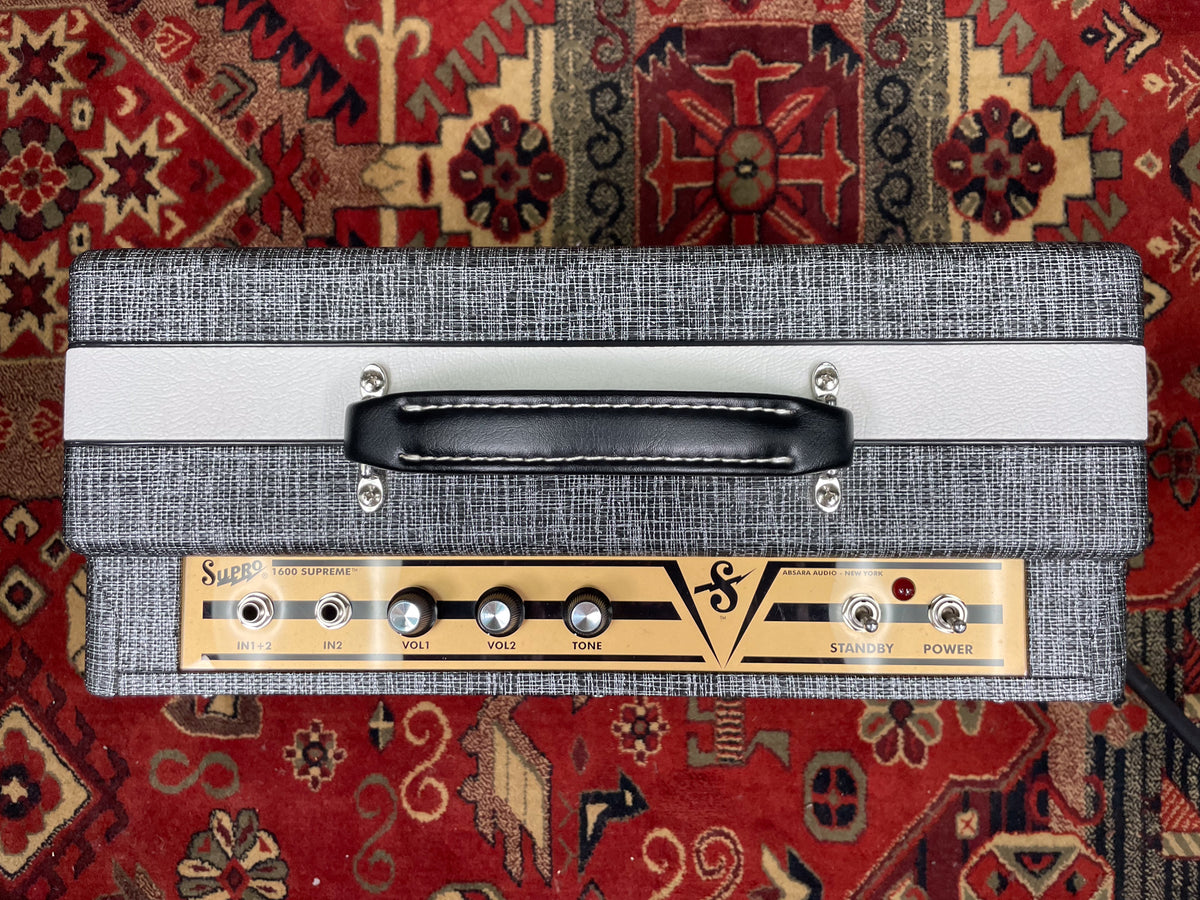 Top-down view of a grey tweed amp head with a black handle, light grey stripe, and gold control panel with black knobs.