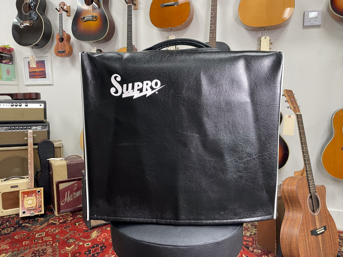 Front view of a black vinyl amplifier cover with white piping, showing some creases and a white logo.
