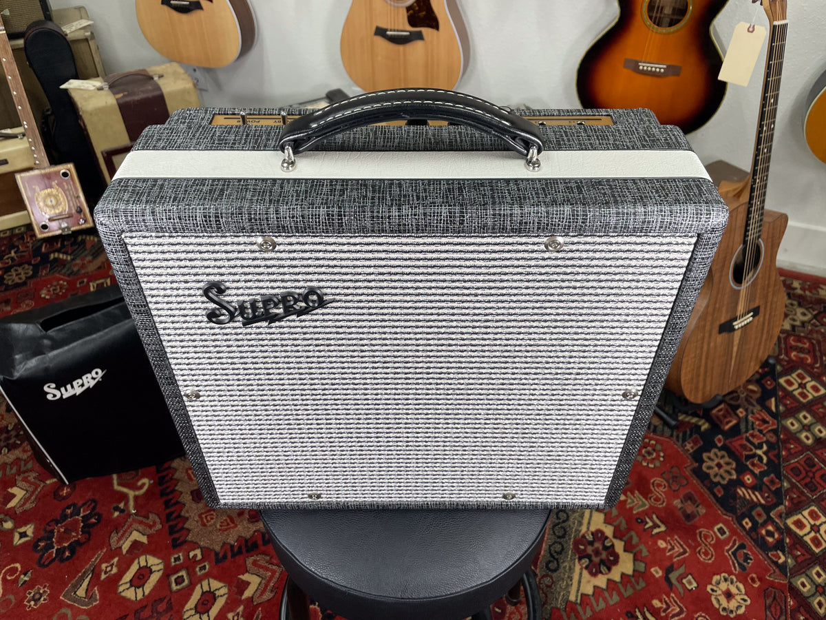 Front view of a Supro combo amp in dark gray tweed with a white stripe and a black and white striped grille.