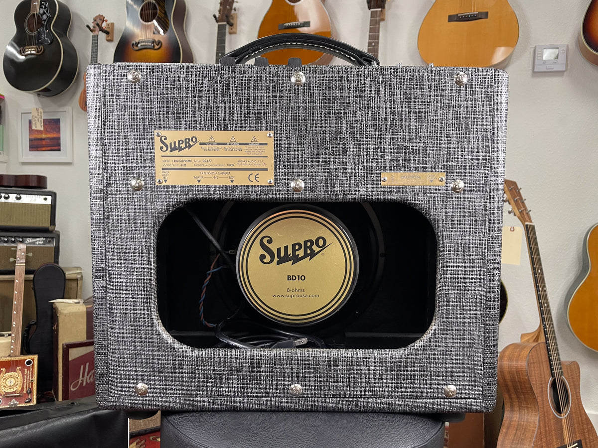 Front view of a Supro combo amp in black and white tweed, revealing a gold speaker with black lettering.