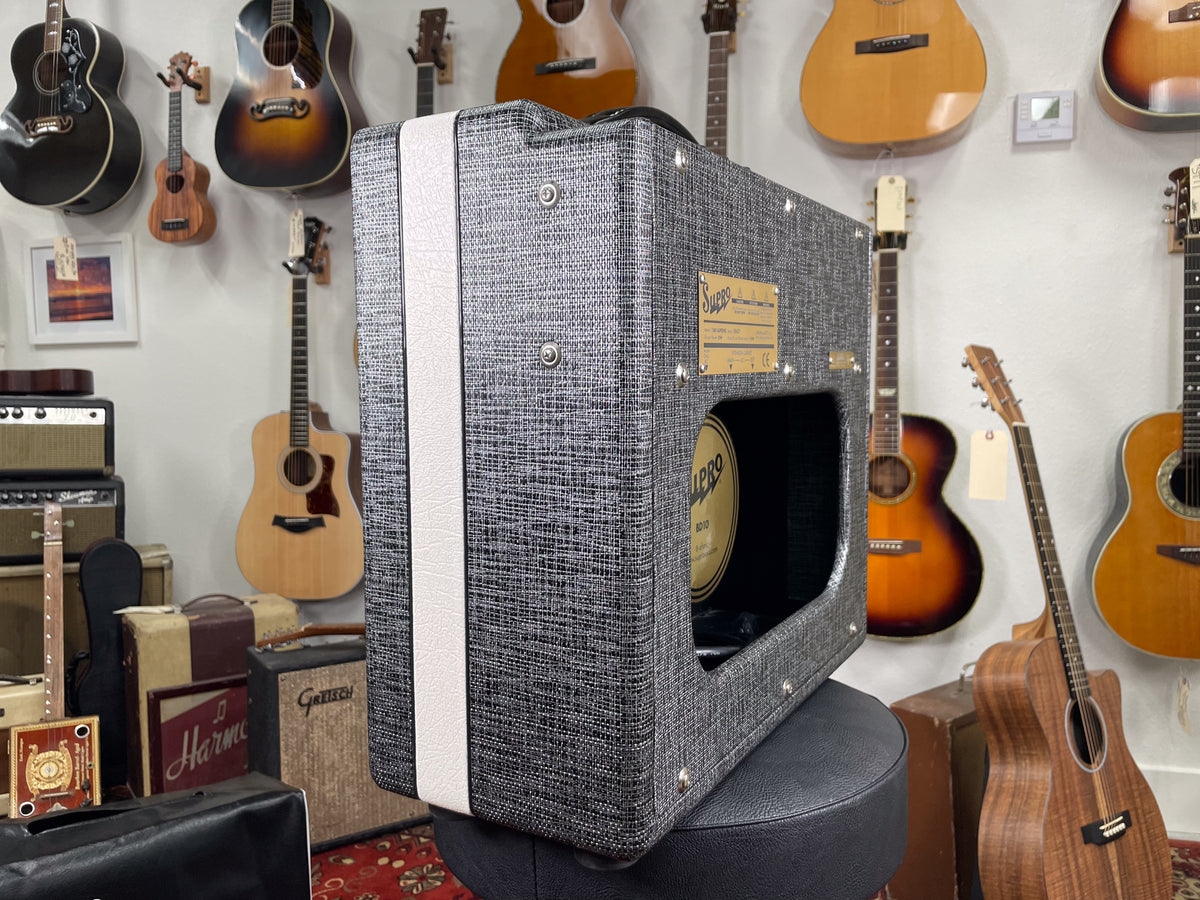 The amp, covered in gray tweed with a white stripe, is angled to show its right side and open back.
