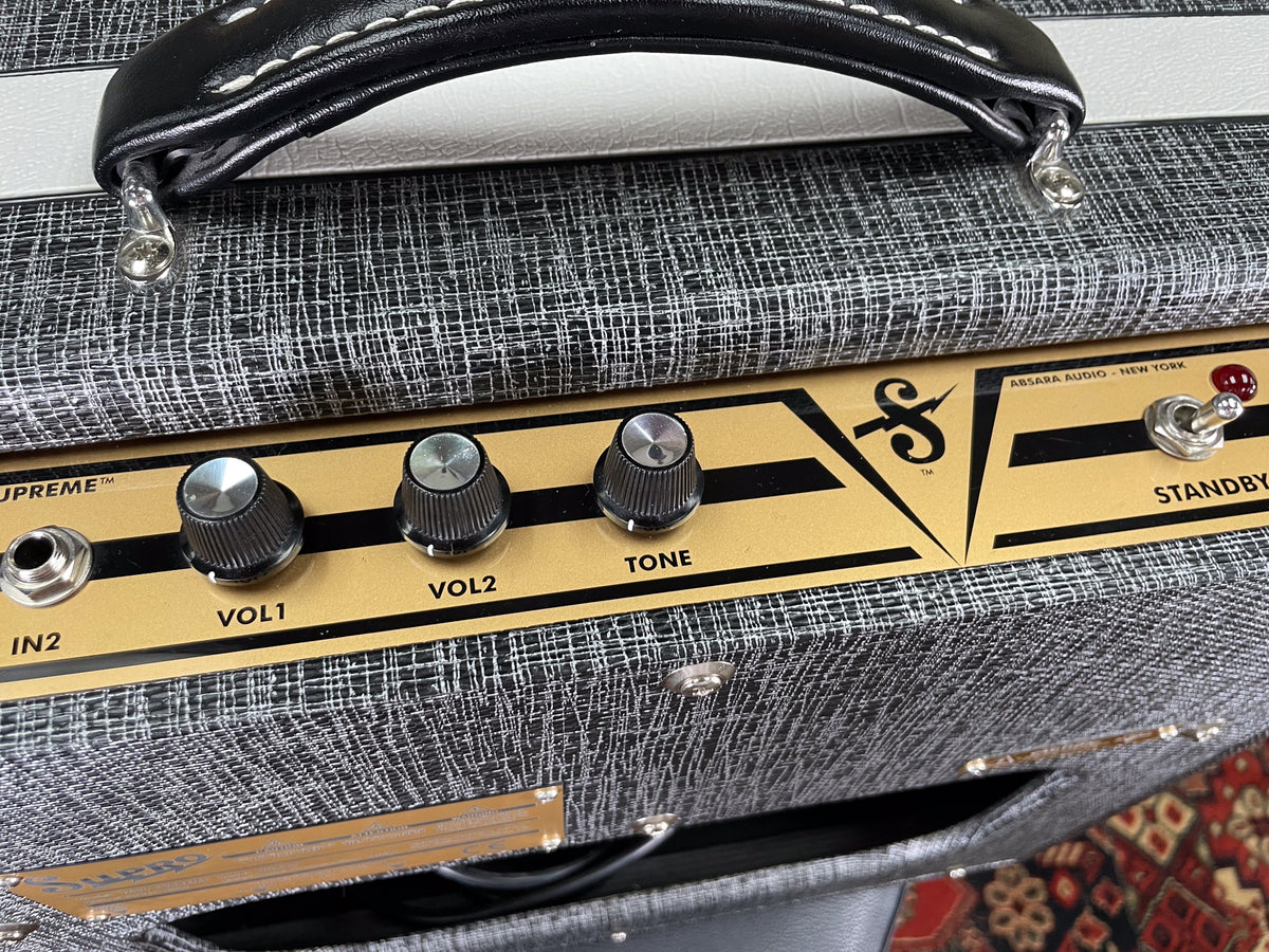 Close-up of the amp's top, showing a black leather handle, gray tweed covering, and a gold control panel with three black knobs and a red standby switch.