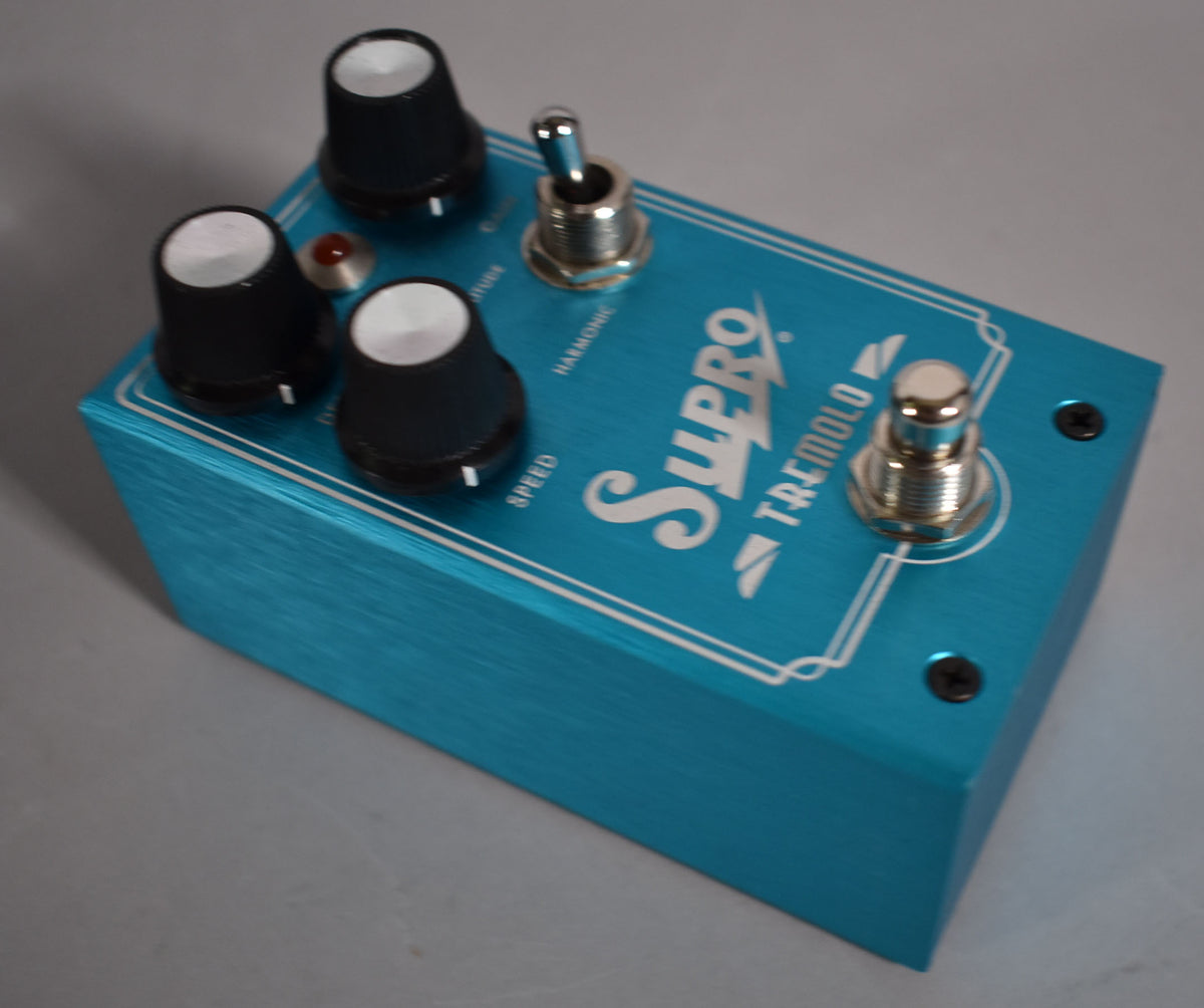 Overhead view of a brushed teal pedal with three black knobs, a red LED, a toggle switch, and a footswitch.