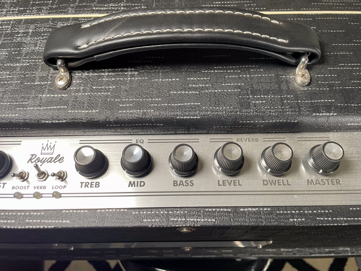 Top-down view of a black amp with a textured finish, showing the leather handle and a silver control panel with six knobs and three toggle switches.