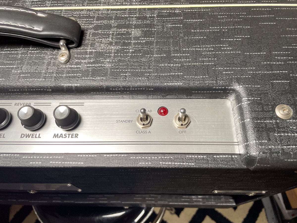 Close-up of the amp's top, showing a black leather handle, brushed metal control panel with three knobs, two toggle switches, and a red indicator light.