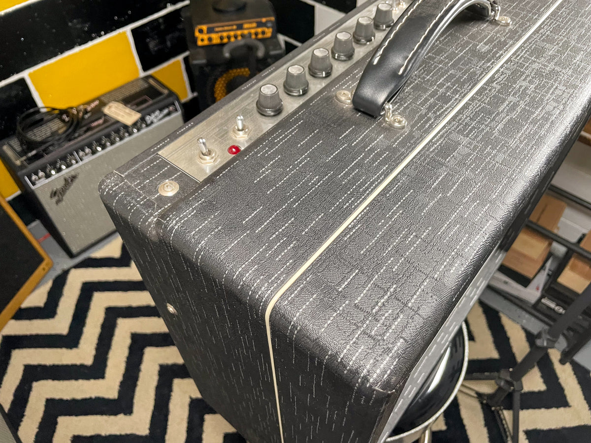 Top-down view of a dark grey textured amp with white piping, showing the control panel with silver knobs and a red indicator light.