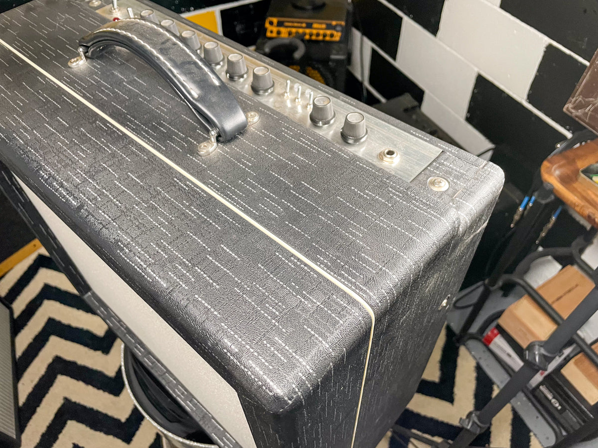 Top-down view of a dark gray amp with white flecked tolex, a silver control panel with six knobs, and a black leather handle.