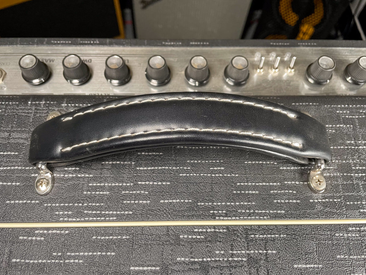 Close-up of the amp's black leather handle with white stitching, mounted on the textured black tolex, with silver control panel and knobs above.
