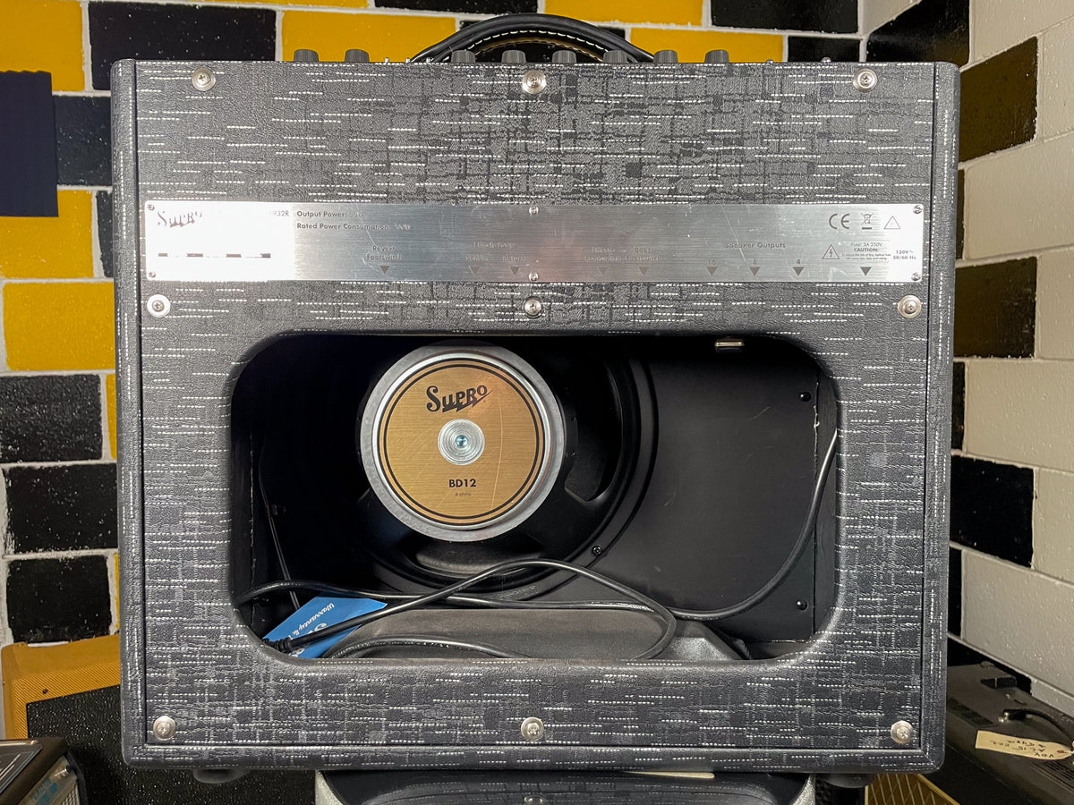 Rear view of a black textured combo amp with an open back, revealing a gold-coned speaker and a silver metal control panel.