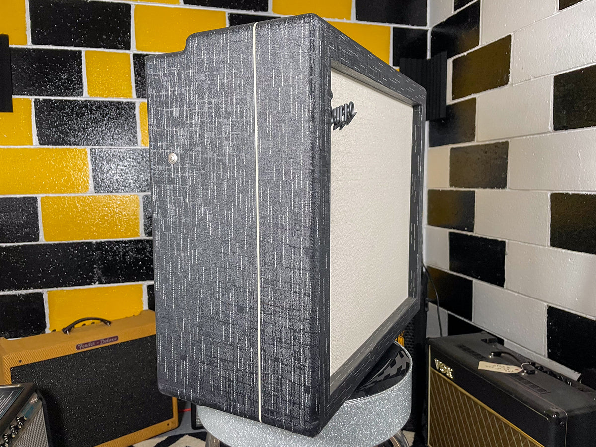 The combo amp is angled, showing its dark gray textured tweed covering, white piping, and a light gray grille cloth.